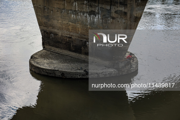 A young boy is sitting on the pillar of a bridge as he is catching fish in Sopore, Jammu and Kashmir, India, on August 18, 2024. 