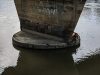 A young boy is sitting on the pillar of a bridge as he is catching fish in Sopore, Jammu and Kashmir, India, on August 18, 2024. (