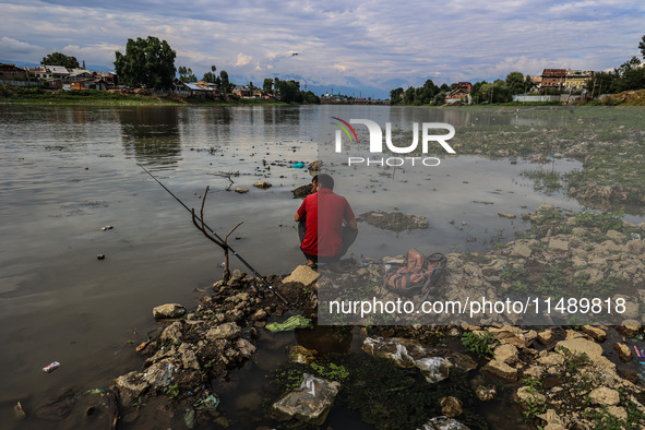 A young man is sitting on the semi-dried portion of River Jhelum as he catches fish in Sopore, Jammu and Kashmir, India, on August 18, 2024....