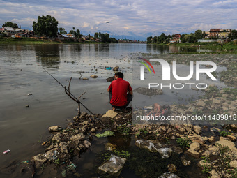 A young man is sitting on the semi-dried portion of River Jhelum as he catches fish in Sopore, Jammu and Kashmir, India, on August 18, 2024....