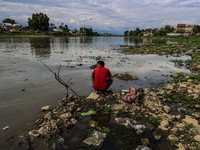 A young man is sitting on the semi-dried portion of River Jhelum as he catches fish in Sopore, Jammu and Kashmir, India, on August 18, 2024....