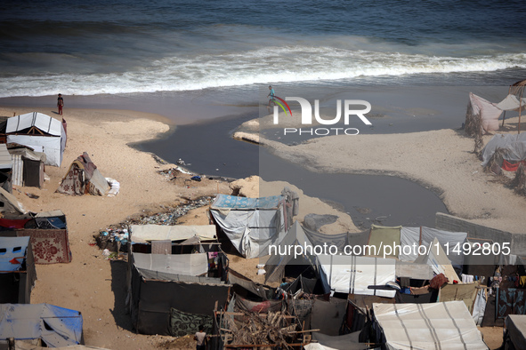 Palestinian displaced people are crossing a beach flooded with sewage water next to their tents in Deir al-Balah in central Gaza Strip, on A...