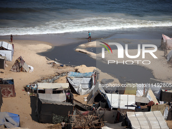 Palestinian displaced people are crossing a beach flooded with sewage water next to their tents in Deir al-Balah in central Gaza Strip, on A...