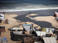 Palestinian displaced people are crossing a beach flooded with sewage water next to their tents in Deir al-Balah in central Gaza Strip, on A...