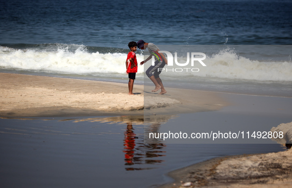 Palestinian displaced people are crossing a beach flooded with sewage water next to their tents in Deir al-Balah in central Gaza Strip, on A...