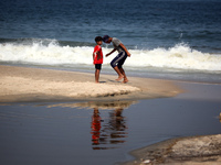 Palestinian displaced people are crossing a beach flooded with sewage water next to their tents in Deir al-Balah in central Gaza Strip, on A...