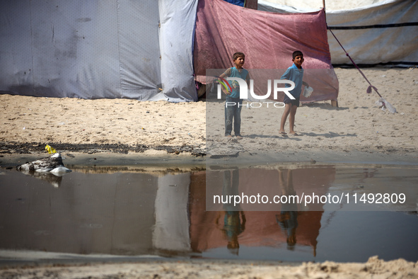 Palestinian displaced people are crossing a beach flooded with sewage water next to their tents in Deir al-Balah in central Gaza Strip, on A...