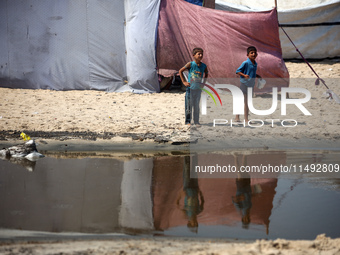 Palestinian displaced people are crossing a beach flooded with sewage water next to their tents in Deir al-Balah in central Gaza Strip, on A...