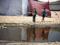 Palestinian displaced people are crossing a beach flooded with sewage water next to their tents in Deir al-Balah in central Gaza Strip, on A...