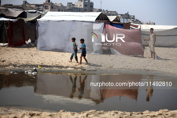 Palestinian displaced people are crossing a beach flooded with sewage water next to their tents in Deir al-Balah in central Gaza Strip, on A...