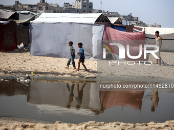 Palestinian displaced people are crossing a beach flooded with sewage water next to their tents in Deir al-Balah in central Gaza Strip, on A...