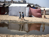 Palestinian displaced people are crossing a beach flooded with sewage water next to their tents in Deir al-Balah in central Gaza Strip, on A...