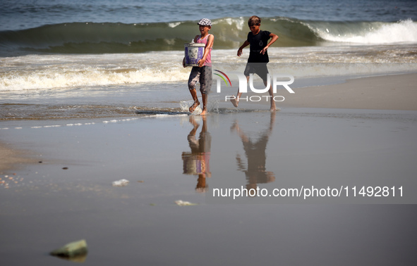 Palestinian displaced people are crossing a beach flooded with sewage water next to their tents in Deir al-Balah in central Gaza Strip, on A...