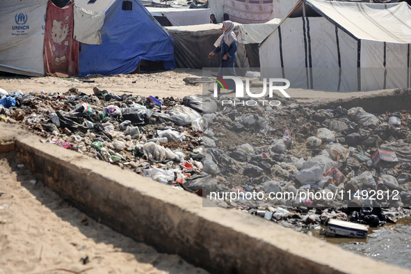 A displaced Palestinian woman is walking beside sewage water and a garbage dump in Deir al-Balah in central Gaza Strip on August 19, 2024, a...