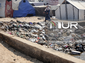 A displaced Palestinian woman is walking beside sewage water and a garbage dump in Deir al-Balah in central Gaza Strip on August 19, 2024, a...