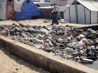 A displaced Palestinian woman is walking beside sewage water and a garbage dump in Deir al-Balah in central Gaza Strip on August 19, 2024, a...