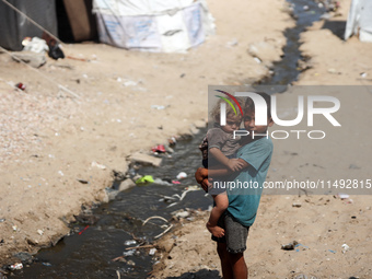 A displaced Palestinian boy is carrying his younger brother while standing next to their tent near the beach in Deir al-Balah in the central...