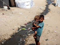 A displaced Palestinian boy is carrying his younger brother while standing next to their tent near the beach in Deir al-Balah in the central...