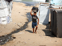 A displaced Palestinian boy is carrying kitchen utensils on his head and walking beside tents near the beach in Deir al-Balah in the central...