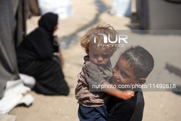 A displaced Palestinian boy is carrying his younger brother while standing next to their tent near the beach in Deir al-Balah in the central...