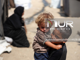 A displaced Palestinian boy is carrying his younger brother while standing next to their tent near the beach in Deir al-Balah in the central...