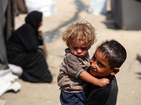 A displaced Palestinian boy is carrying his younger brother while standing next to their tent near the beach in Deir al-Balah in the central...