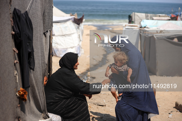 A displaced Palestinian mother is carrying her son, who is suffering from a skin rash, while standing next to a pool of sewage water on the...