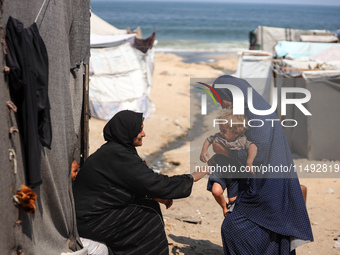 A displaced Palestinian mother is carrying her son, who is suffering from a skin rash, while standing next to a pool of sewage water on the...