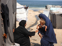 A displaced Palestinian mother is carrying her son, who is suffering from a skin rash, while standing next to a pool of sewage water on the...