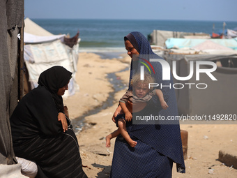 A displaced Palestinian mother is carrying her son, who is suffering from a skin rash, while standing next to a pool of sewage water on the...