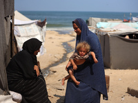 A displaced Palestinian mother is carrying her son, who is suffering from a skin rash, while standing next to a pool of sewage water on the...