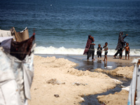 Palestinian displaced people are crossing a beach flooded with sewage water next to their tents in Deir al-Balah in central Gaza Strip, on A...