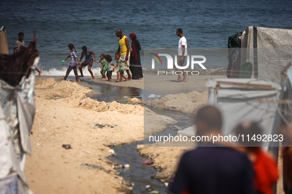 Palestinian displaced people are crossing a beach flooded with sewage water next to their tents in Deir al-Balah in central Gaza Strip, on A...