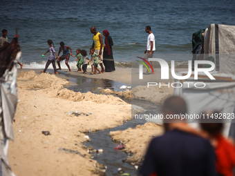 Palestinian displaced people are crossing a beach flooded with sewage water next to their tents in Deir al-Balah in central Gaza Strip, on A...