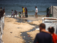 Palestinian displaced people are crossing a beach flooded with sewage water next to their tents in Deir al-Balah in central Gaza Strip, on A...