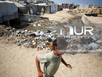 A displaced Palestinian girl is walking beside sewage water and a garbage dump in Deir al-Balah in central Gaza Strip on August 19, 2024, as...