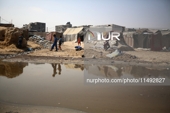 Palestinian displaced people are crossing a beach flooded with sewage water next to their tents in Deir al-Balah in central Gaza Strip, on A...