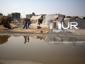 Palestinian displaced people are crossing a beach flooded with sewage water next to their tents in Deir al-Balah in central Gaza Strip, on A...