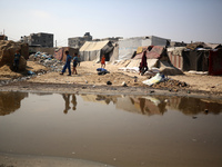 Palestinian displaced people are crossing a beach flooded with sewage water next to their tents in Deir al-Balah in central Gaza Strip, on A...