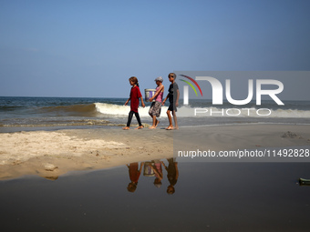 Palestinian displaced people are crossing a beach flooded with sewage water next to their tents in Deir al-Balah in central Gaza Strip, on A...