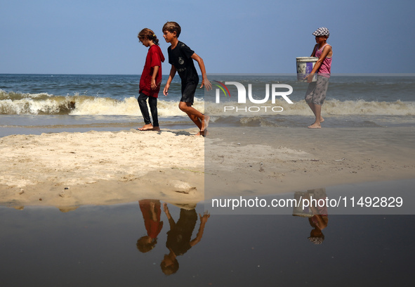 Palestinian displaced people are crossing a beach flooded with sewage water next to their tents in Deir al-Balah in central Gaza Strip, on A...