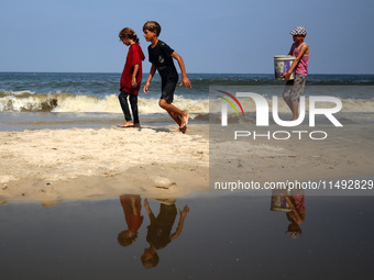 Palestinian displaced people are crossing a beach flooded with sewage water next to their tents in Deir al-Balah in central Gaza Strip, on A...