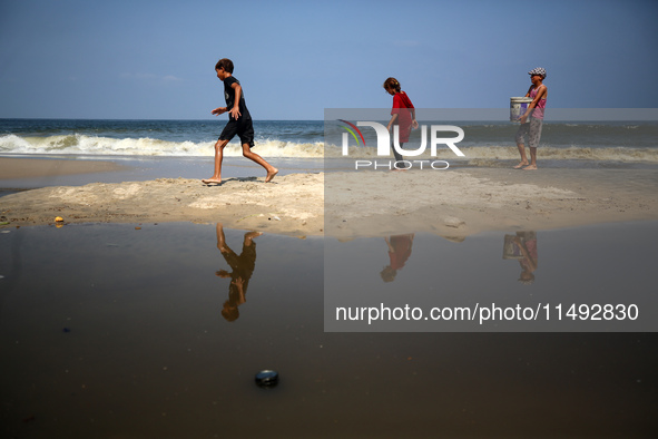 Palestinian displaced people are crossing a beach flooded with sewage water next to their tents in Deir al-Balah in central Gaza Strip, on A...