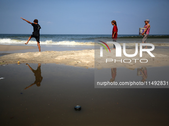 Palestinian displaced people are crossing a beach flooded with sewage water next to their tents in Deir al-Balah in central Gaza Strip, on A...