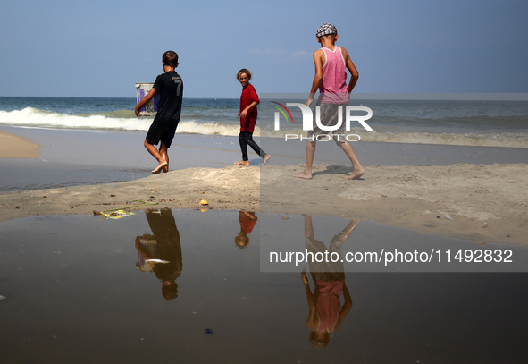 Palestinian displaced people are crossing a beach flooded with sewage water next to their tents in Deir al-Balah in central Gaza Strip, on A...