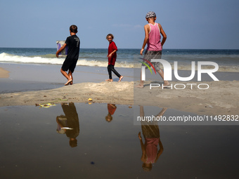 Palestinian displaced people are crossing a beach flooded with sewage water next to their tents in Deir al-Balah in central Gaza Strip, on A...