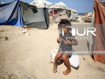 A displaced Palestinian girl is sitting beside the tents in Deir al-Balah in central Gaza Strip on August 19, 2024, amid the ongoing conflic...