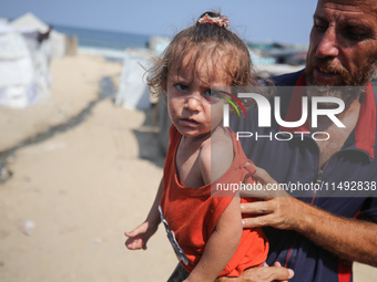 A displaced Palestinian father is carrying his son, who is suffering from a skin rash, while standing next to a pool of sewage water on the...