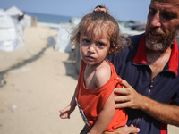 A displaced Palestinian father is carrying his son, who is suffering from a skin rash, while standing next to a pool of sewage water on the...