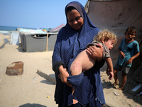 A displaced Palestinian mother is carrying her son, who is suffering from a skin rash, while standing next to a pool of sewage water on the...